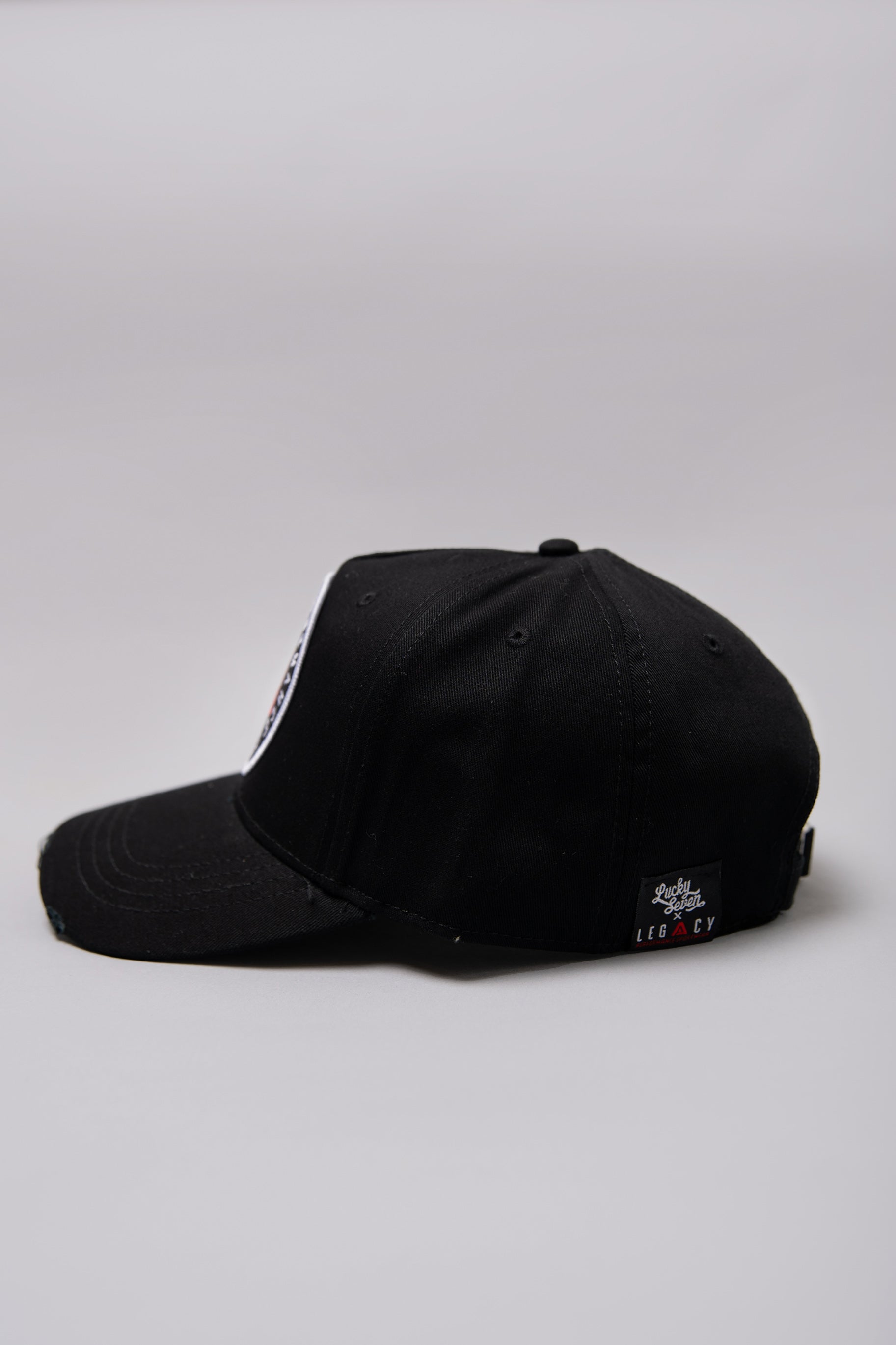 Side view of black Legacy baseball cap with white and red logo.