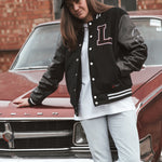 Black letterman jacket with wool body and leather sleeves. Paired with a black and white Legacy trucker cap.