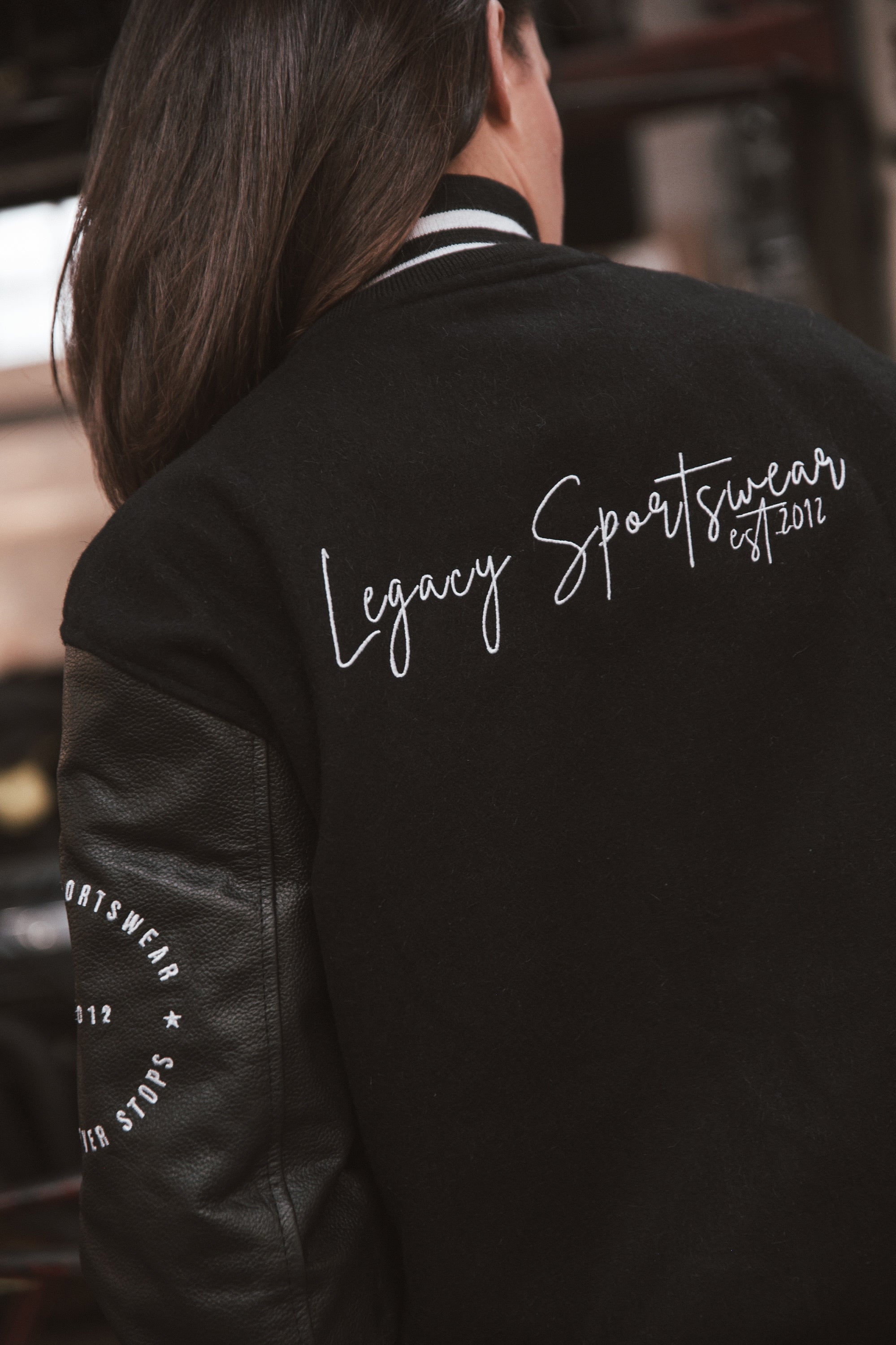 Legacy Sportswear written in white on back of black letterman jacket with wool body and leather sleeves.