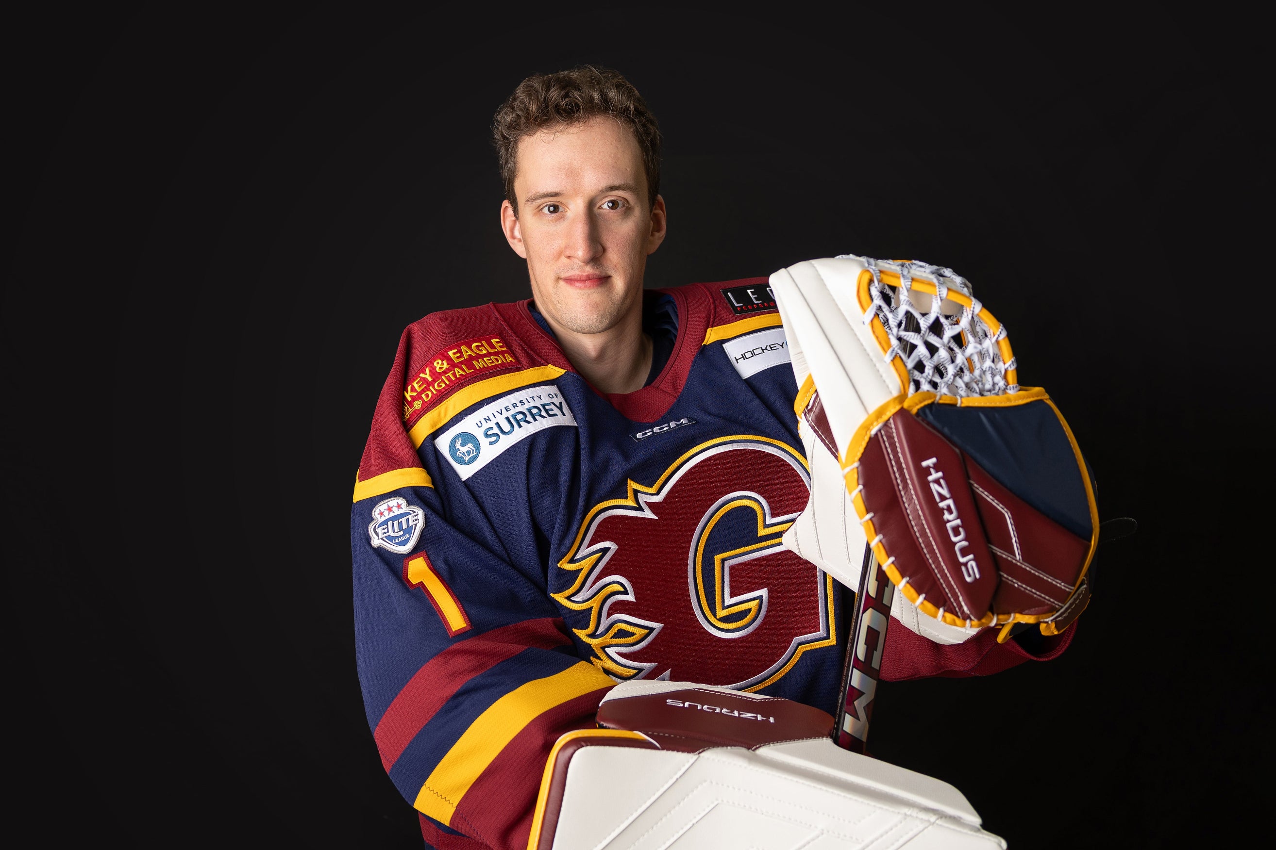 Person wearing a hockey jersey with a glove and stick, on a black background