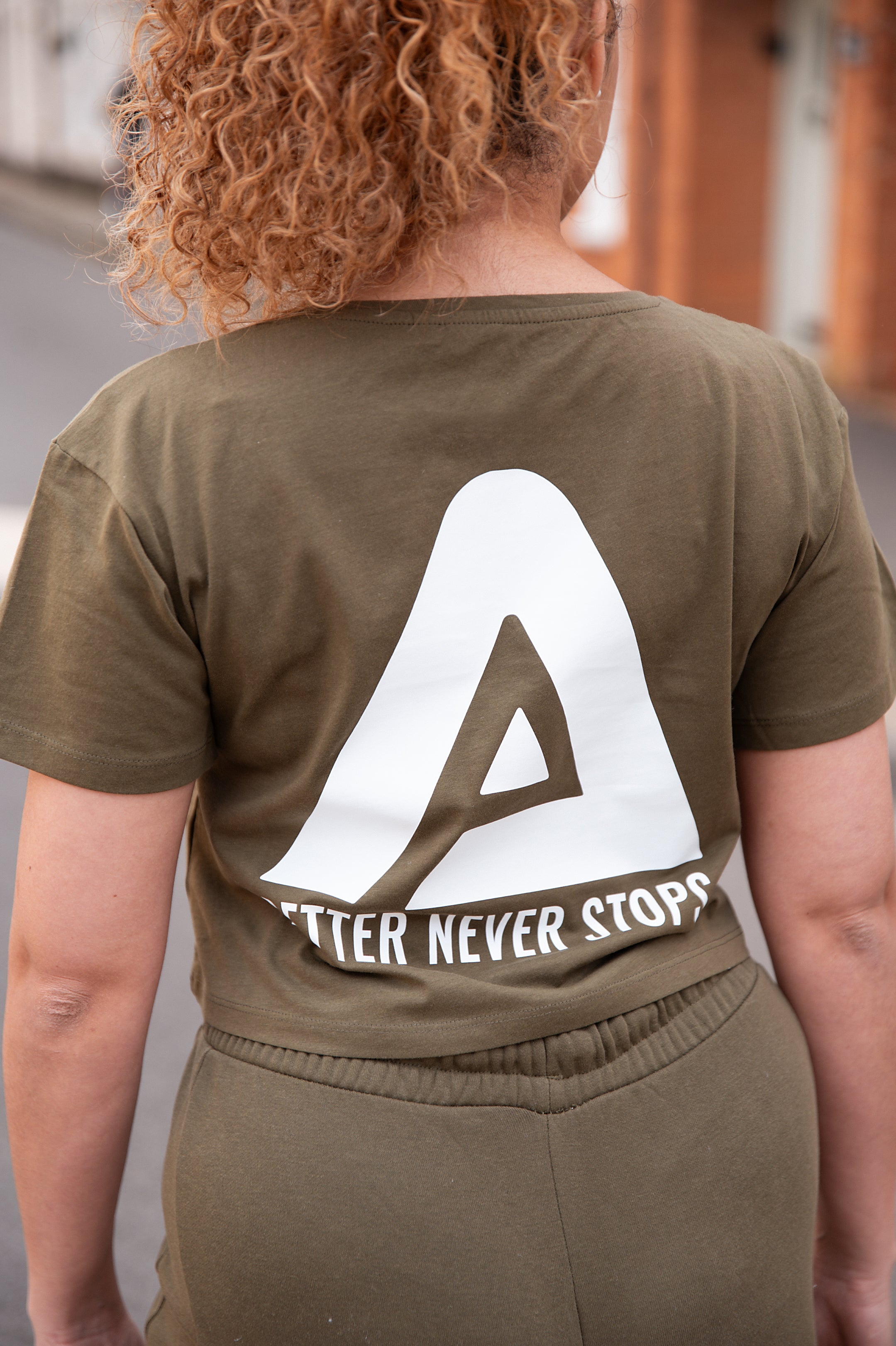 Back view of women's olive crop t-shirt with white Better Never Stops logo.