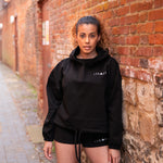 Women's black oversized crop hoodie with tie waist and small white logo.