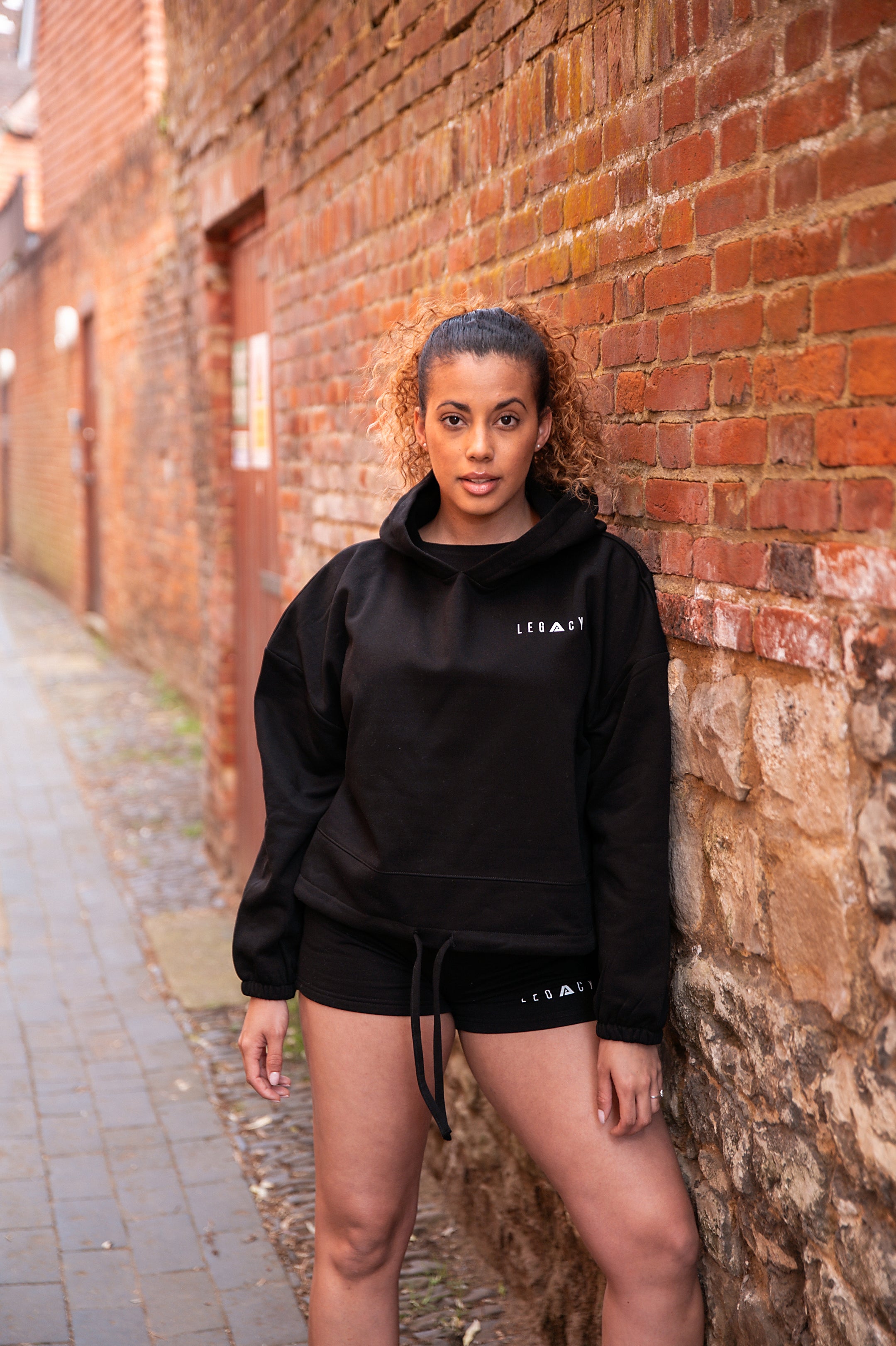 Women's black oversized crop hoodie with tie waist and small white logo.