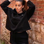 Women's black oversized crop hoodie with tie waist and small white logo.