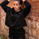 Women's black oversized crop hoodie with tie waist and small white logo.