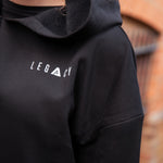 Close up of small white Legacy logo on women's black oversized crop hoodie.