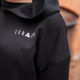 Close up of small white Legacy logo on women's black oversized crop hoodie.