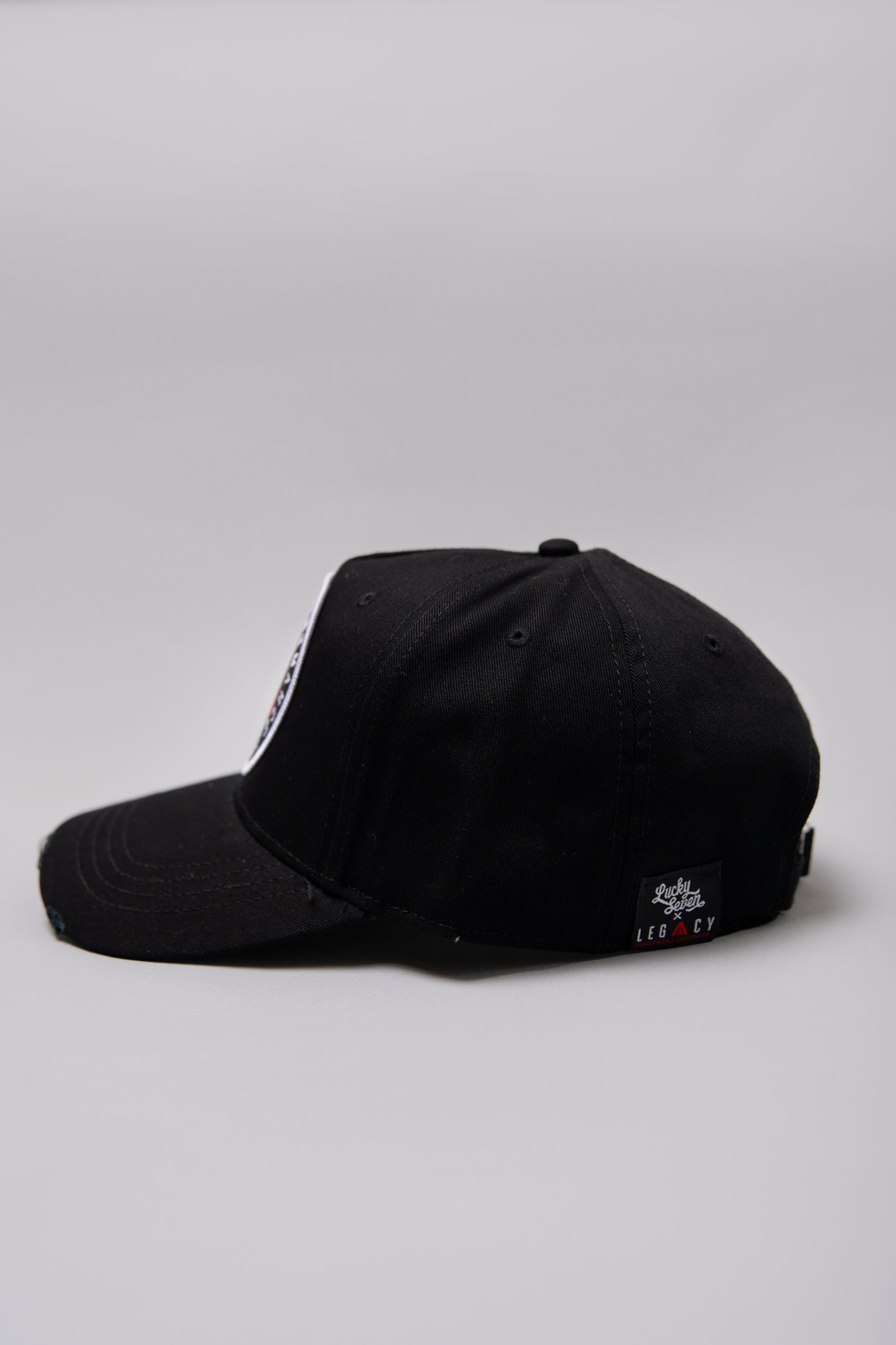 Side view of black Legacy baseball cap with white and red logo. 