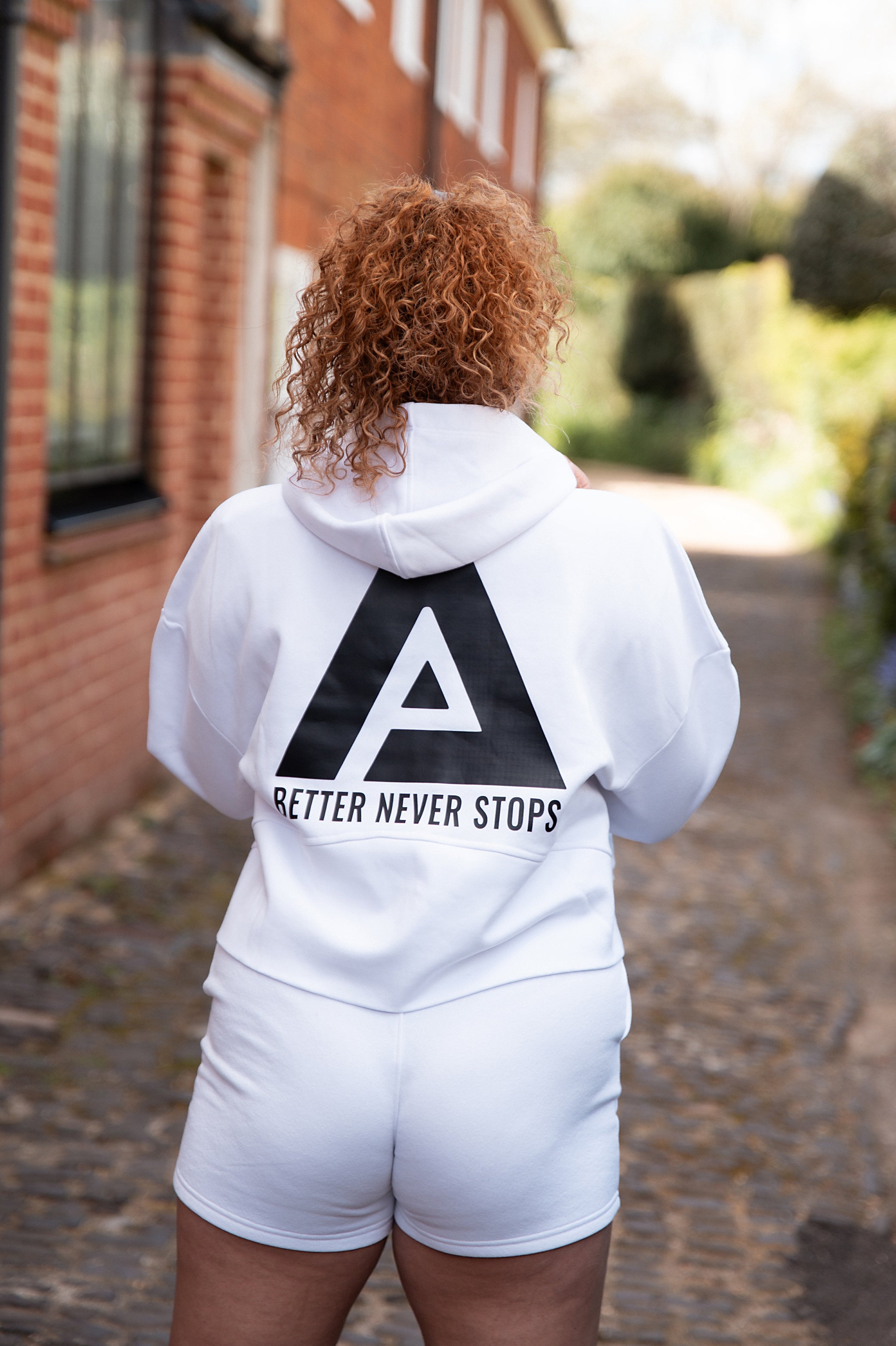 Back view of women's white cropped hoodie with black Better Never Stops logo.