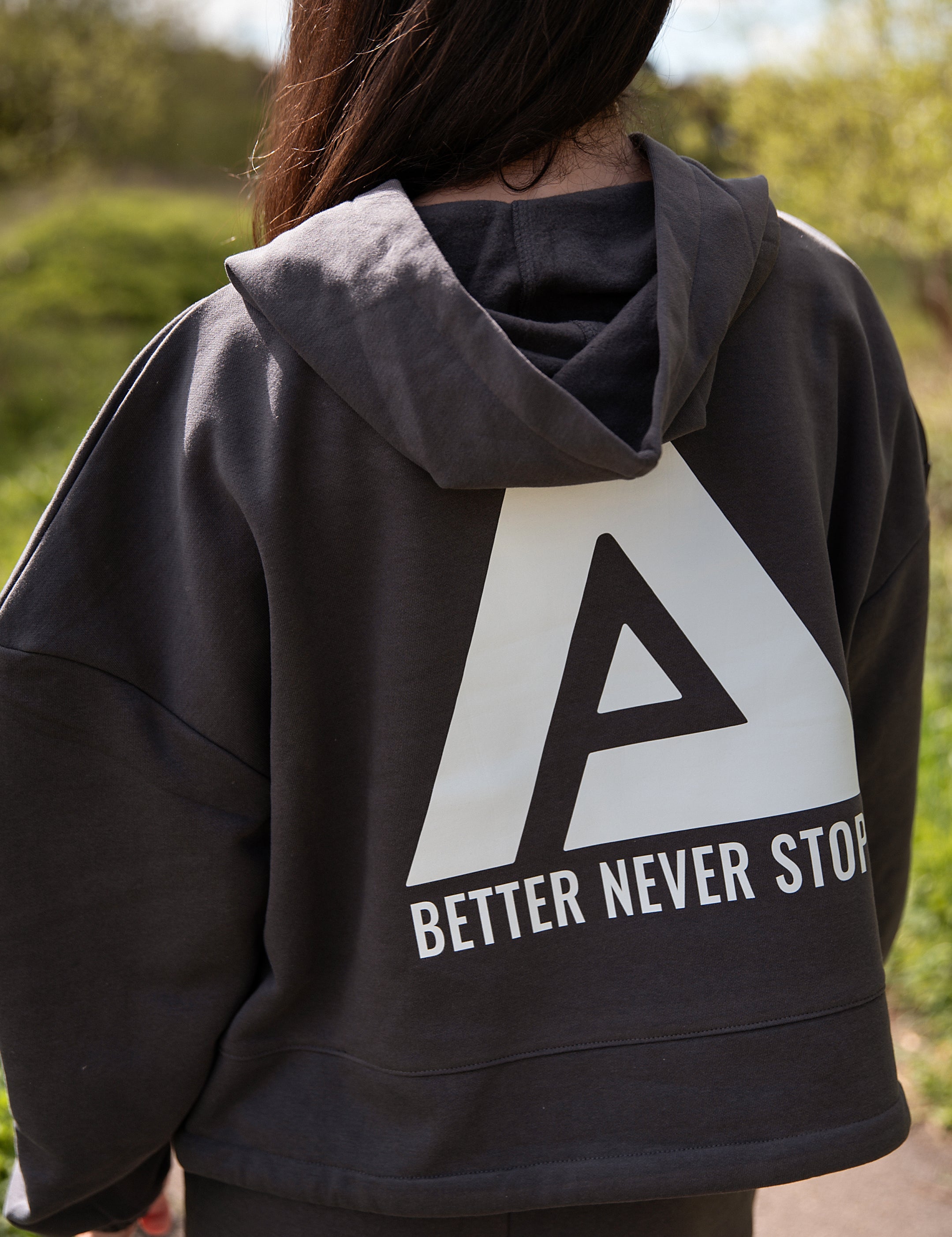 Back view of women's graphite oversized crop hoodie with tie waist and white Better Never Stops logo.
