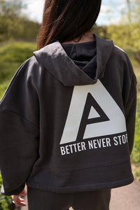 Back view of women's graphite oversized crop hoodie with tie waist and white Better Never Stops logo.