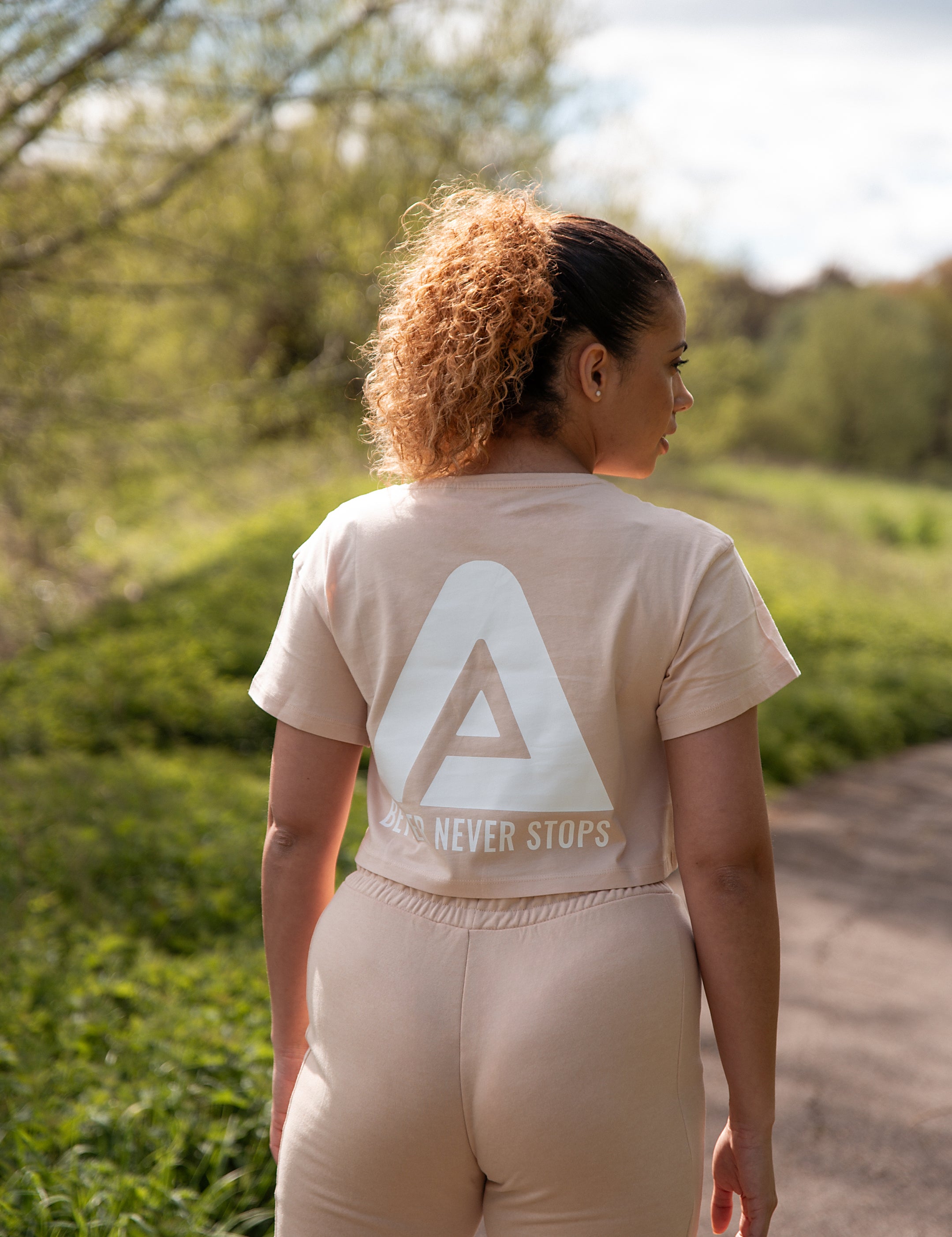 Back view of women's soft pink crop t-shirt with white Better Never Stops logo.