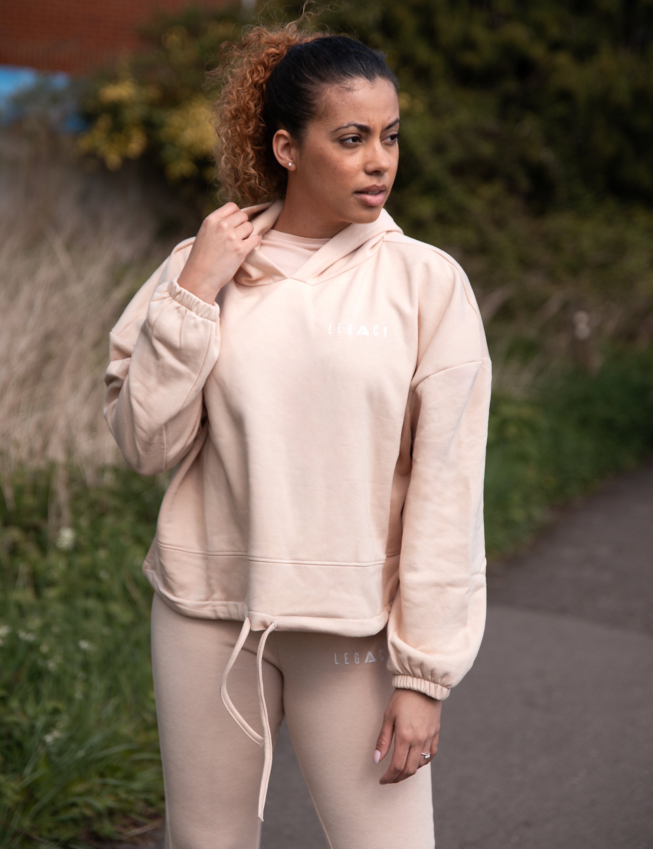 Women's soft pink oversized crop hoodie with tie waist and small white logo.