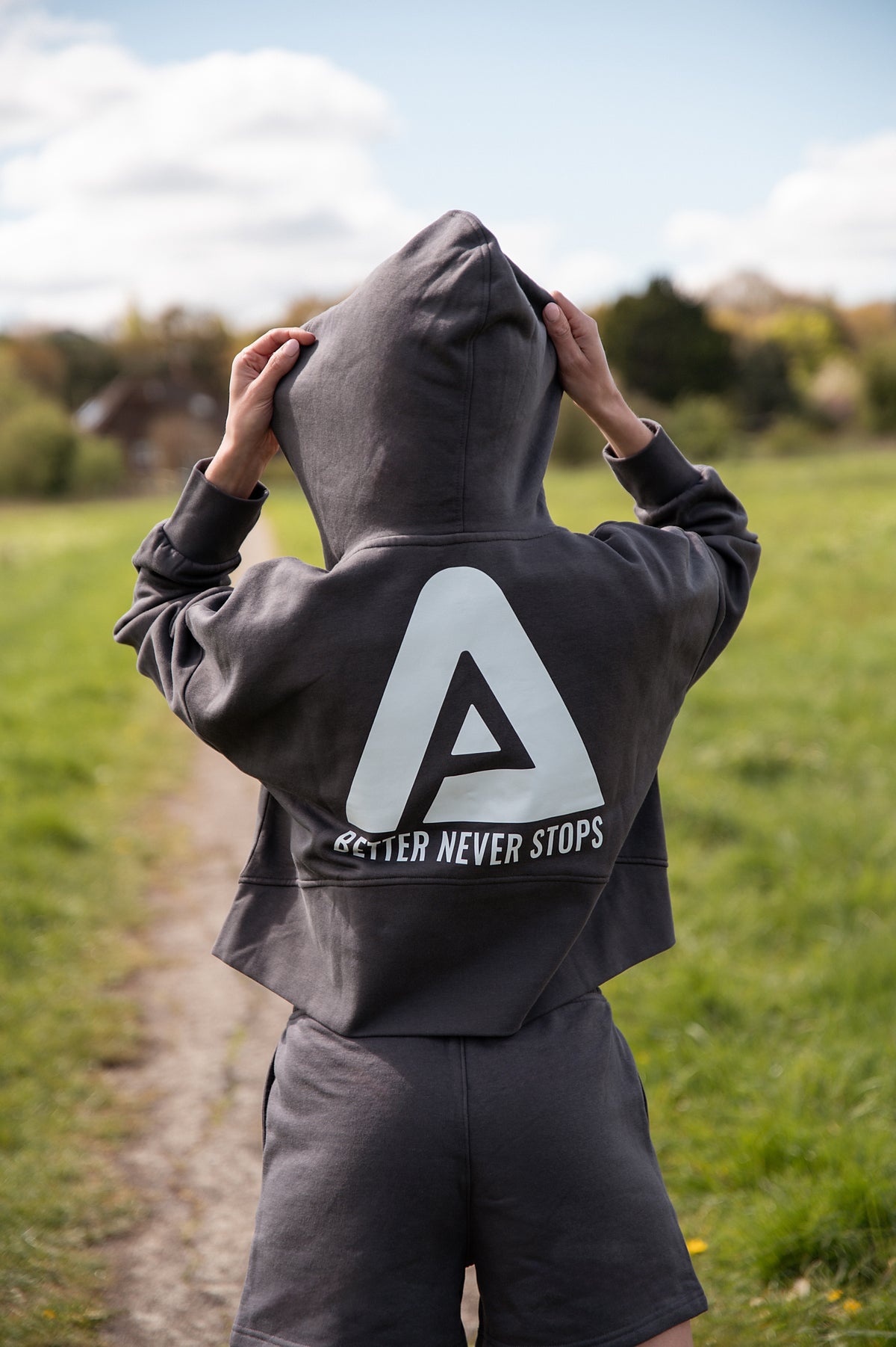 Back view of women's graphite cropped hoodie with white Better Never Stops logo.