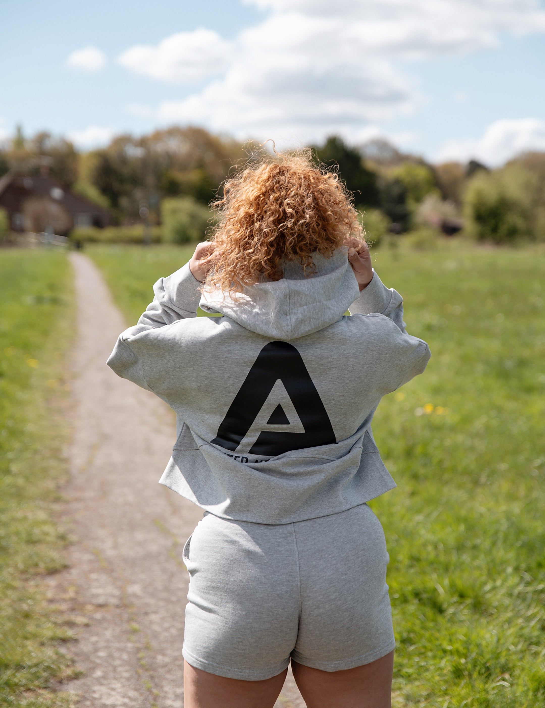 Back view of women's grey oversized crop hoodie with tie waist and black Better Never Stops logo.