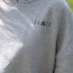 Close up of small black Legacy logo on women's grey oversized crop hoodie.