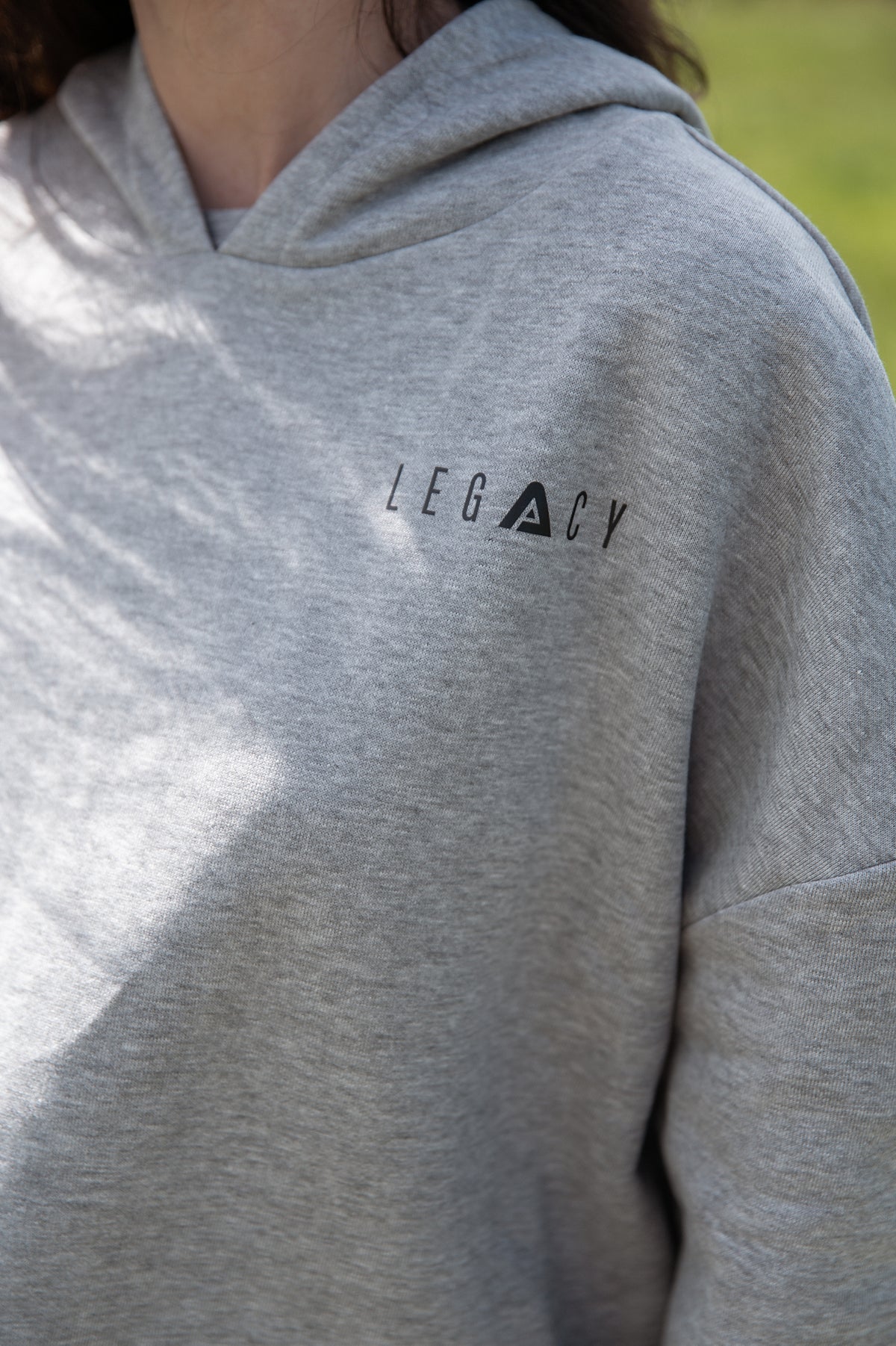 Close up of small black Legacy logo on women's grey oversized crop hoodie.