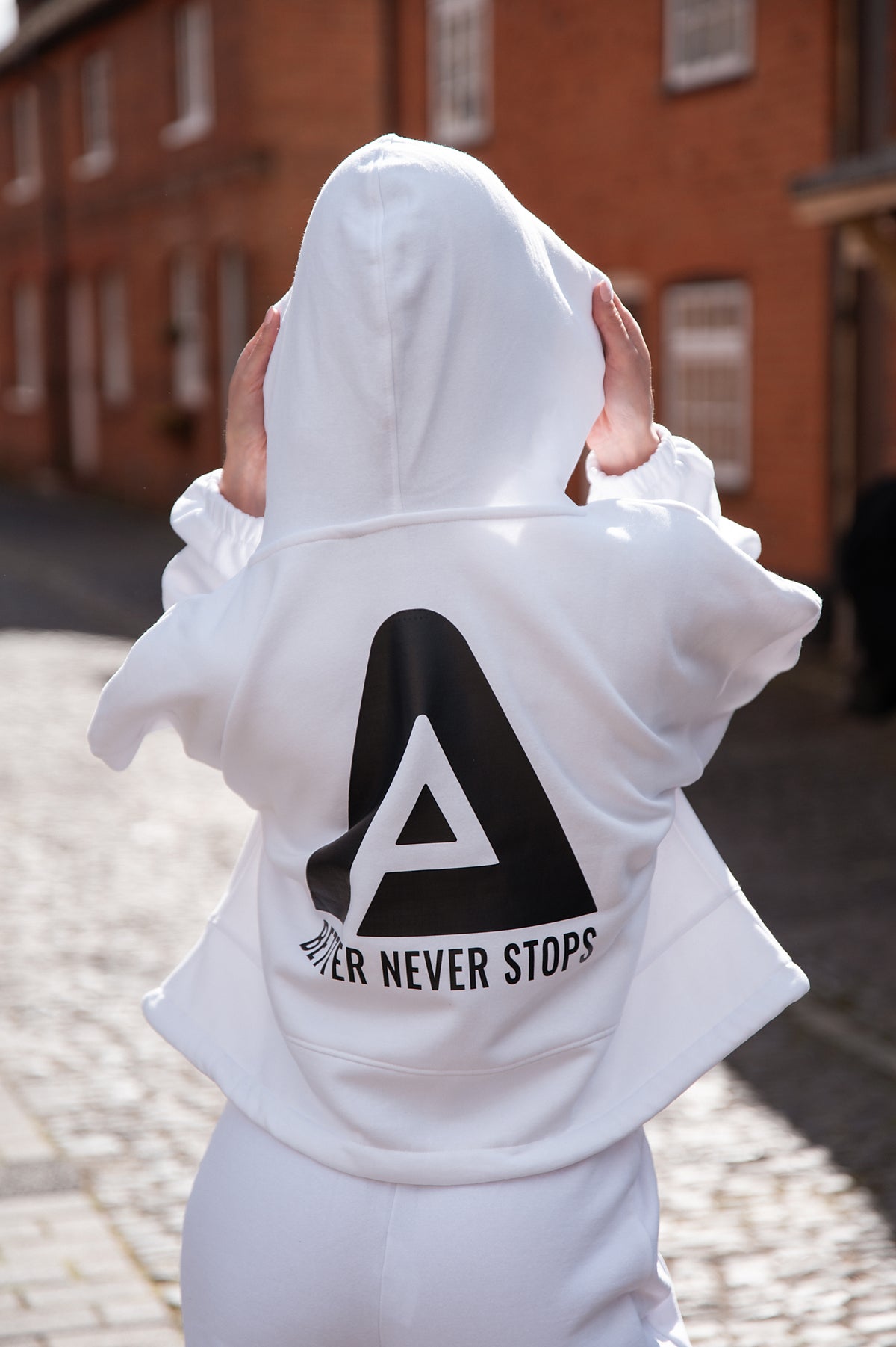 Back view of women's white oversized crop hoodie with tie waist and black Better Never Stops logo.