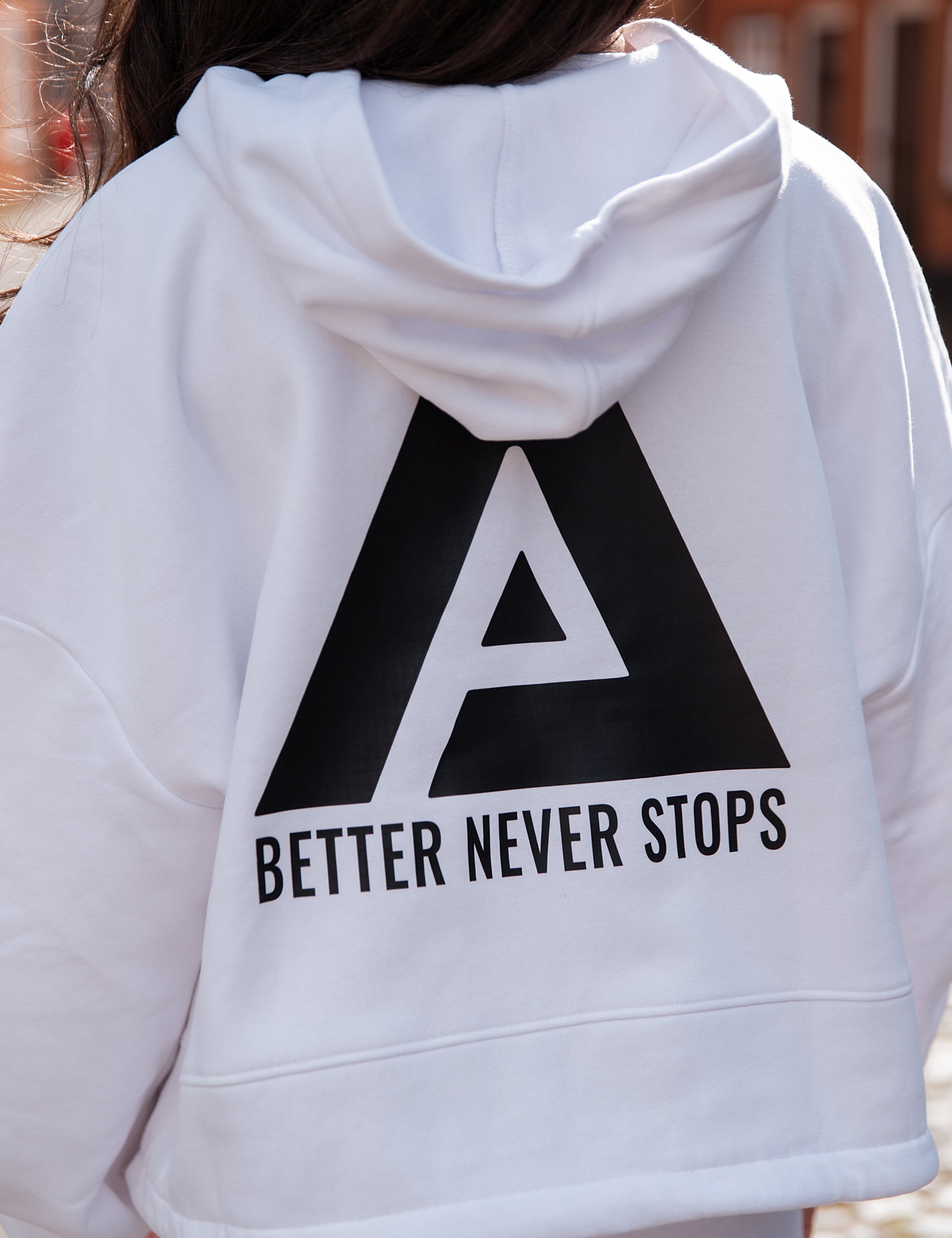 Back view of women's white oversized crop hoodie with tie waist and black Better Never Stops logo.