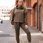 Women's olive oversized crop hoodie with tie waist and small white logo.