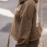 Women's olive oversized crop hoodie with tie waist and white Better Never Stops logo on back.