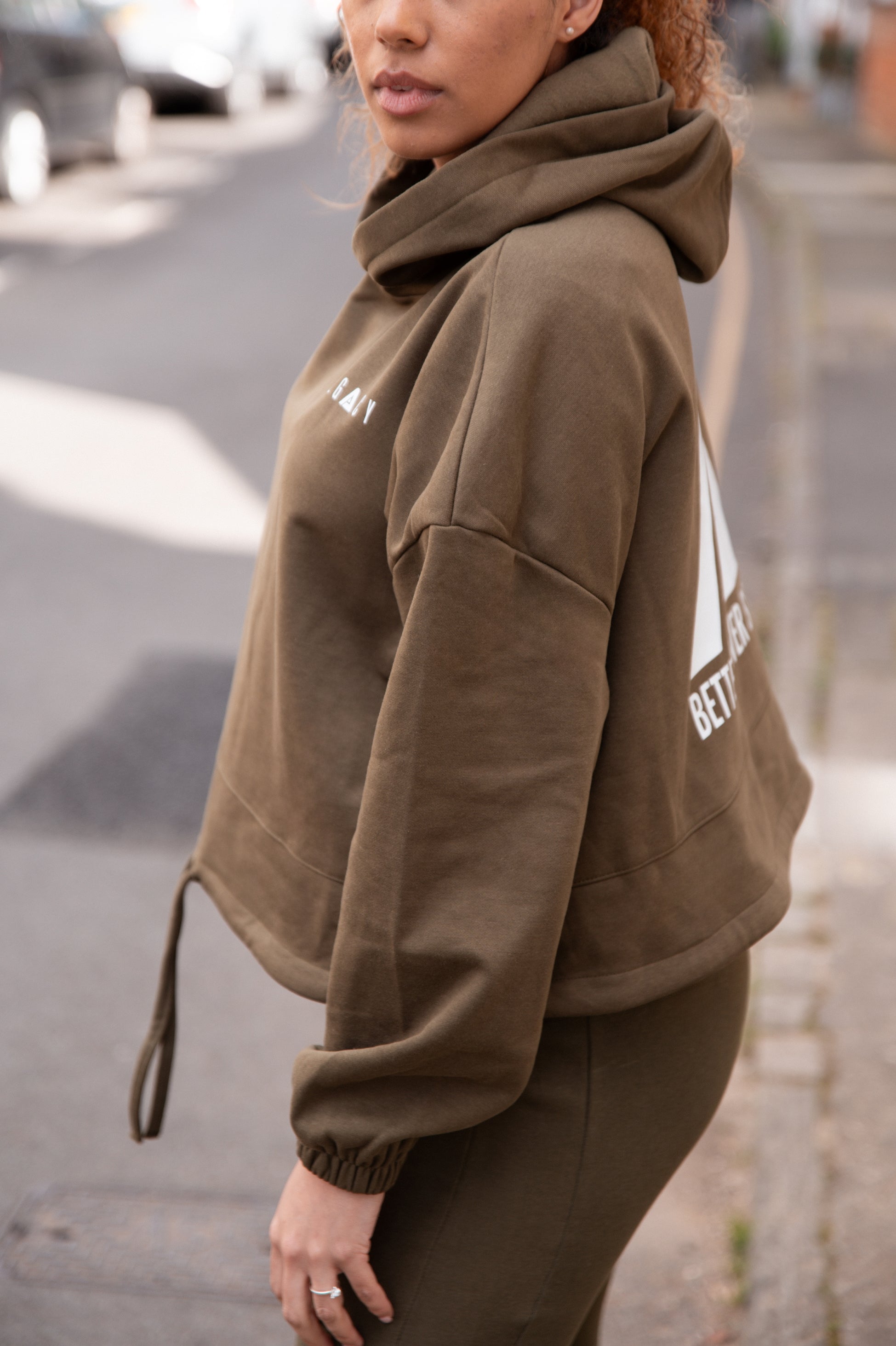 Women's olive oversized crop hoodie with tie waist and white Better Never Stops logo on back.