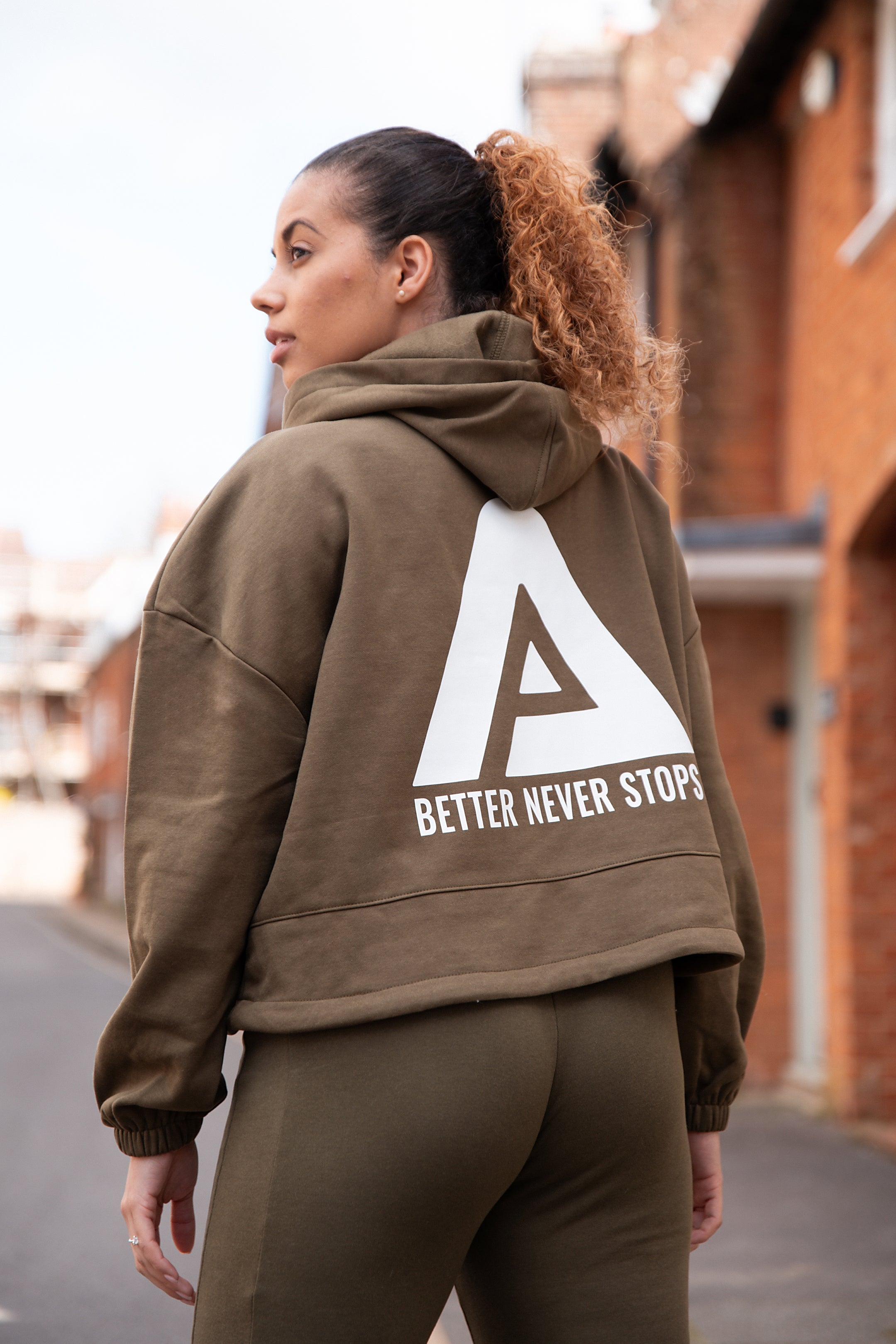 Back view of women's olive oversized crop hoodie with tie waist and white Better Never Stops logo.