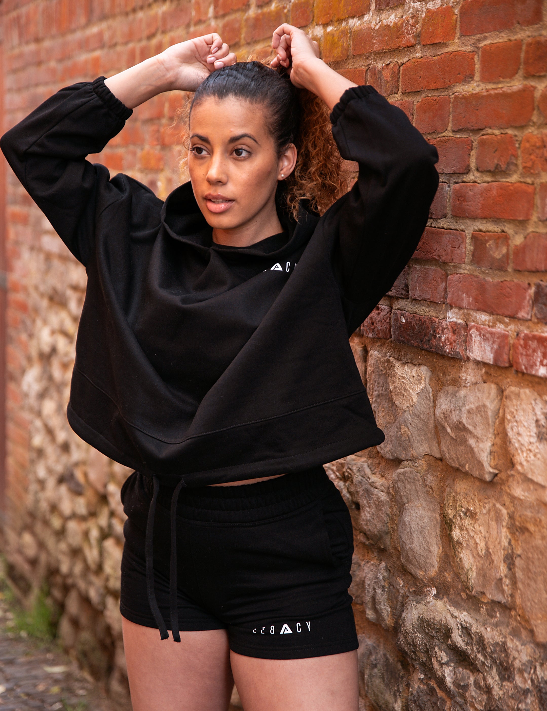 Women's black oversized crop hoodie with tie waist and small white logo.