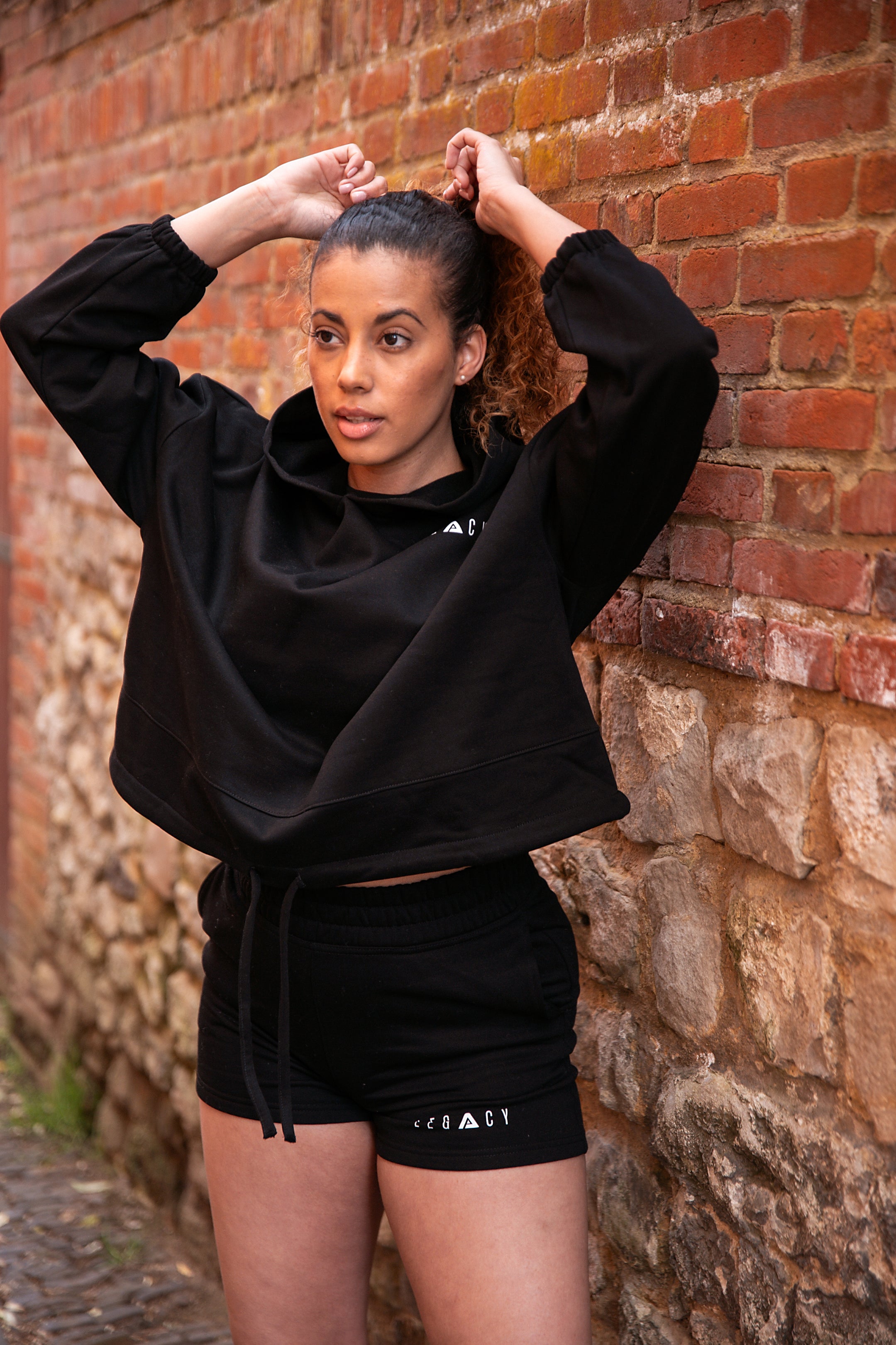 Women's black oversized crop hoodie with tie waist and small white logo.