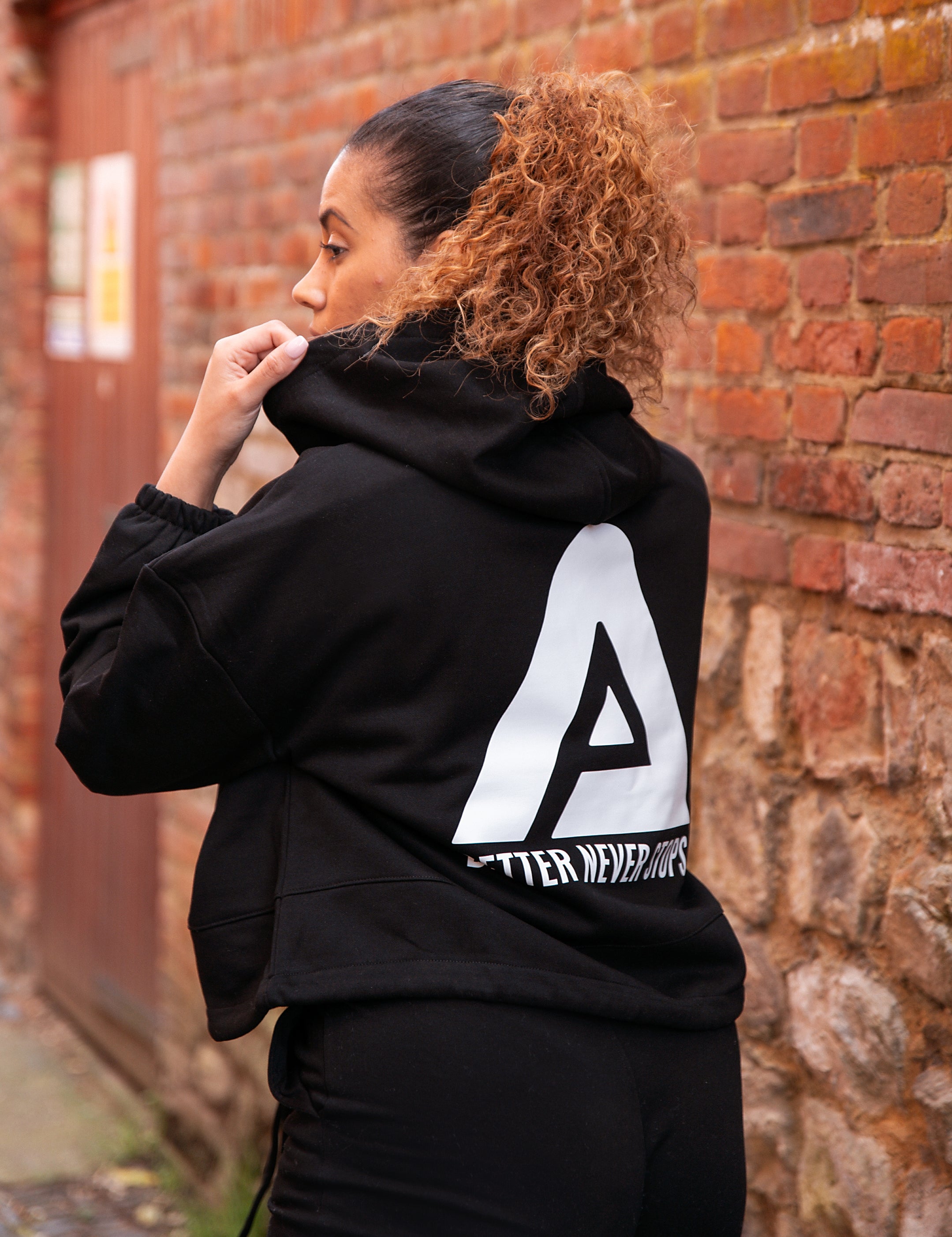 Back view of women's black oversized crop hoodie with tie waist and white Better Never Stops logo.