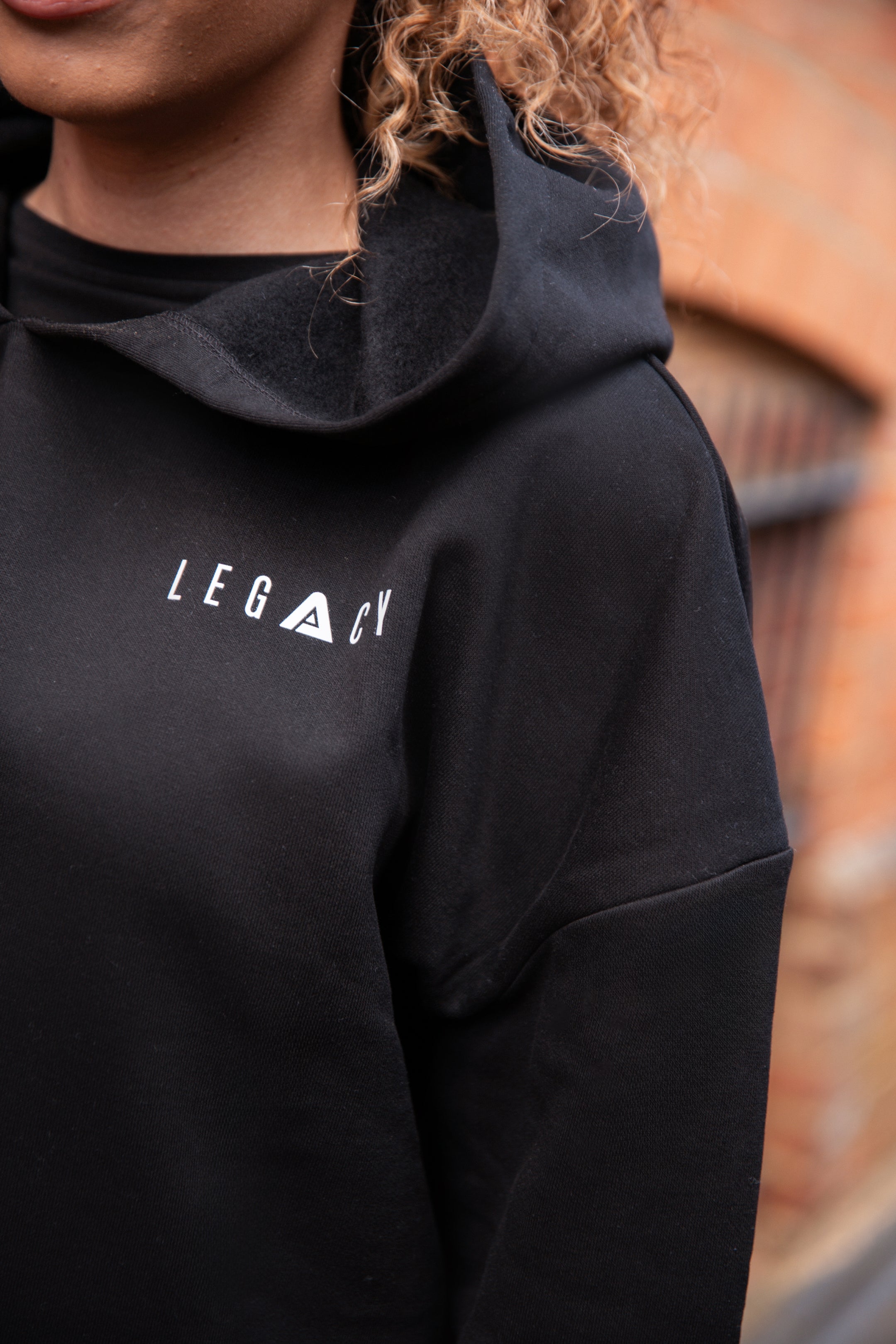 Close up of small white Legacy logo on women's black oversized crop hoodie.