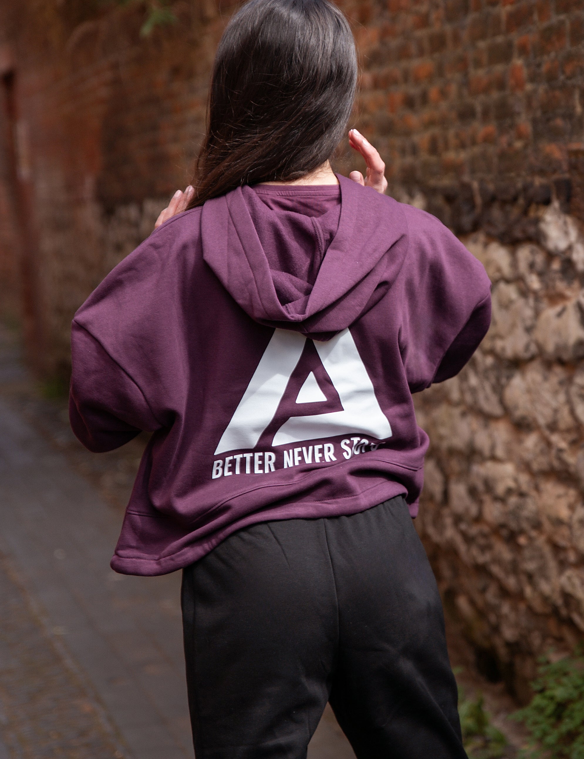 Back view of women's burgundy oversized crop hoodie with tie waist and white Better Never Stops logo.
