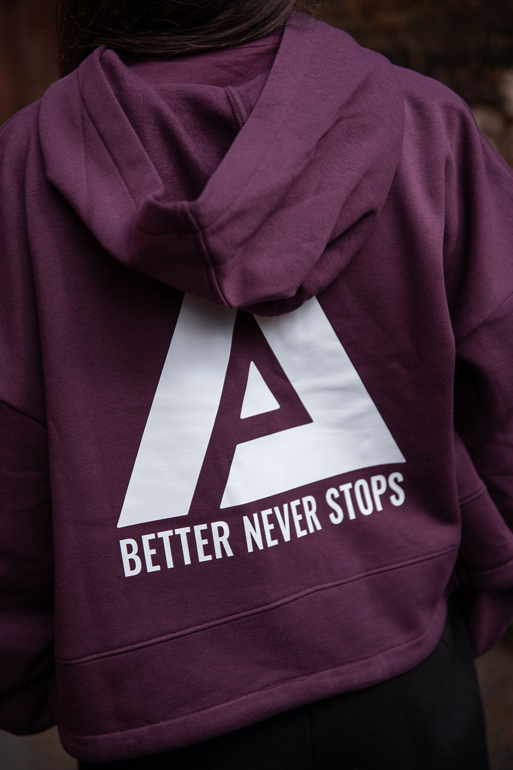 Back view of women's burgundy oversized crop hoodie with tie waist and white Better Never Stops logo.