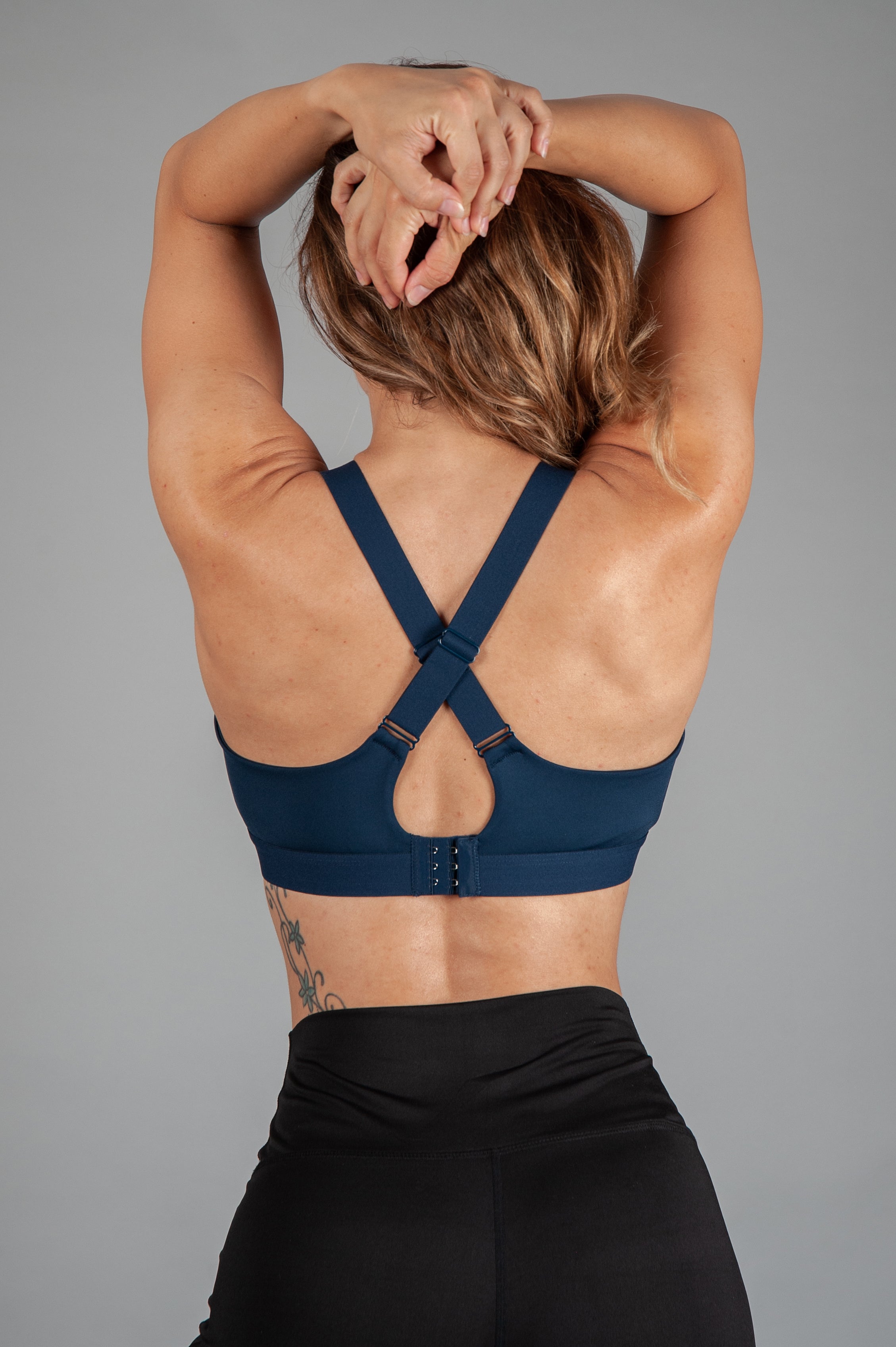 Back view of women's navy sports bra with cross-over adjustable straps and clasp back.