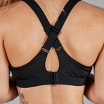Back view of women's black sports bra with cross-over adjustable straps and clasp back.